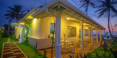 A cozy, well-lit beach house porch at sunset with palm trees.
