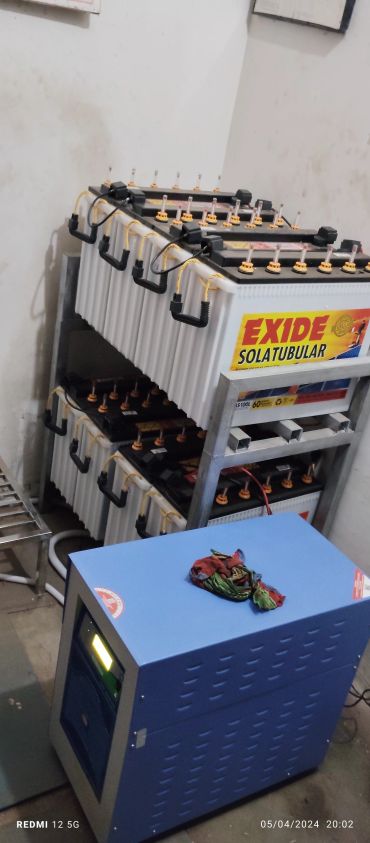 Rack of Exide Solatubular batteries with a blue inverter in a room.