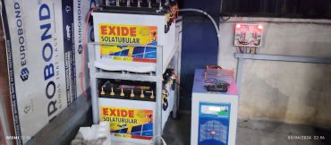 Stacked Exide Solatubular batteries connected to a power inverter in a room.