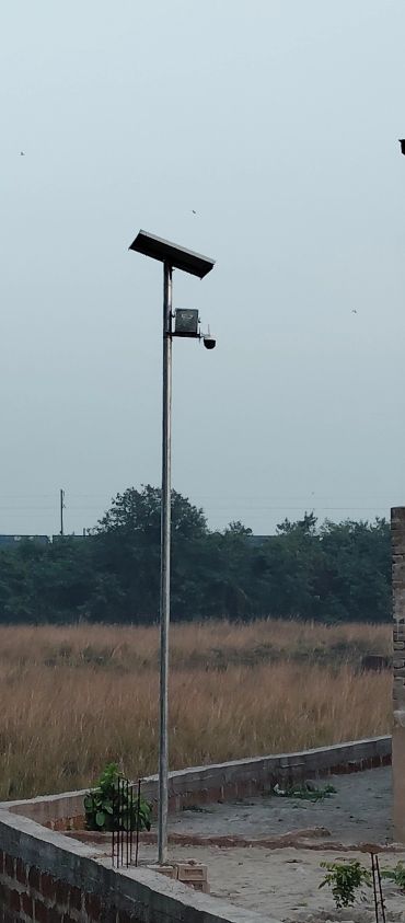A tall solar-powered street light with a security camera in a rural area.