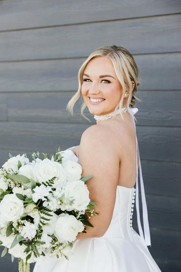 Bride in white dress holding a bouquet of white flowers, smiling at the camera.