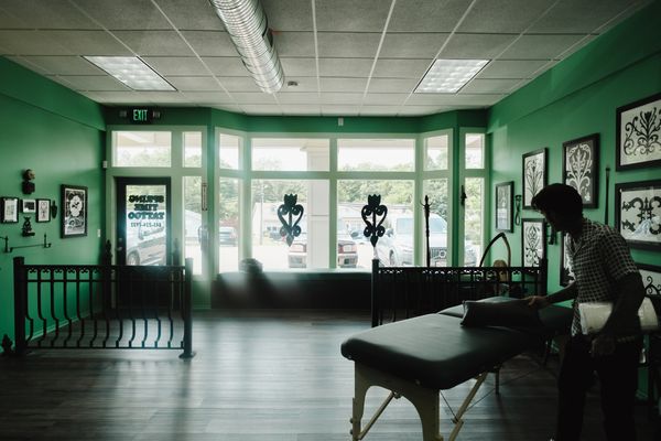 A person setting up a massage table in a green-walled room with large windows.