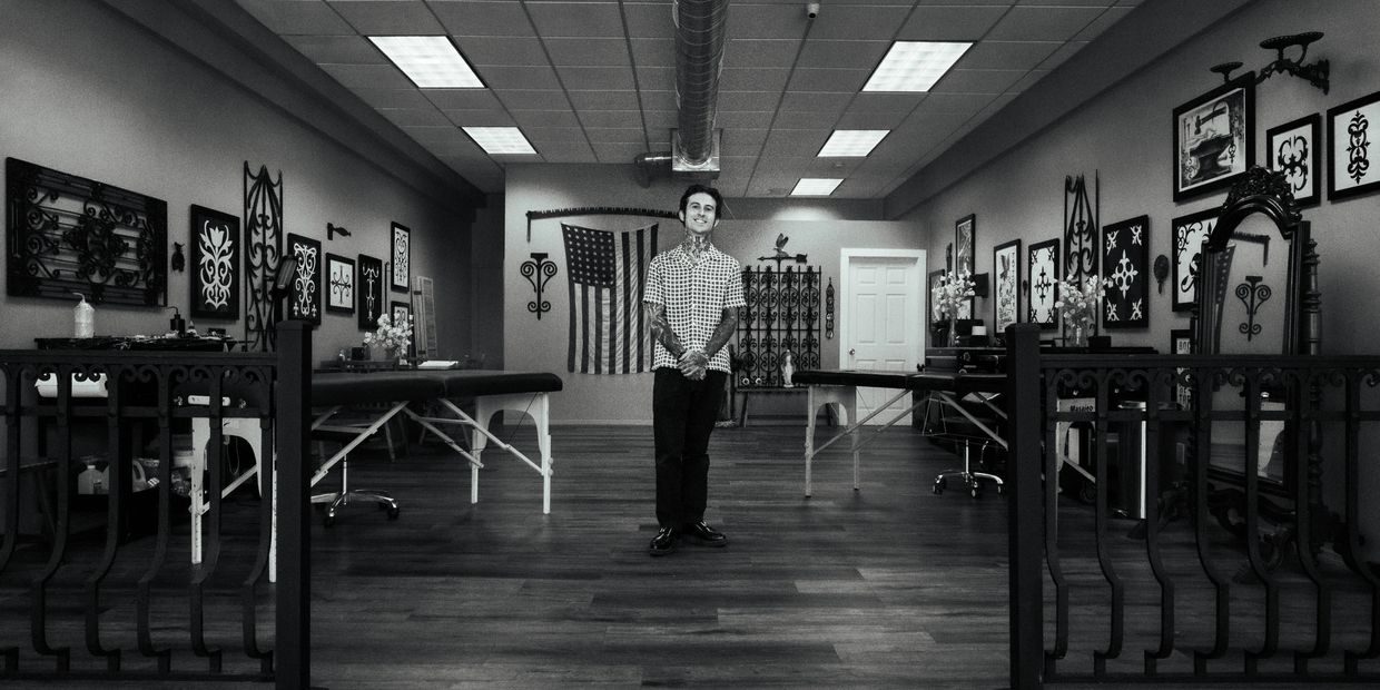 Man standing in a tattoo studio with art and American flag on the wall.