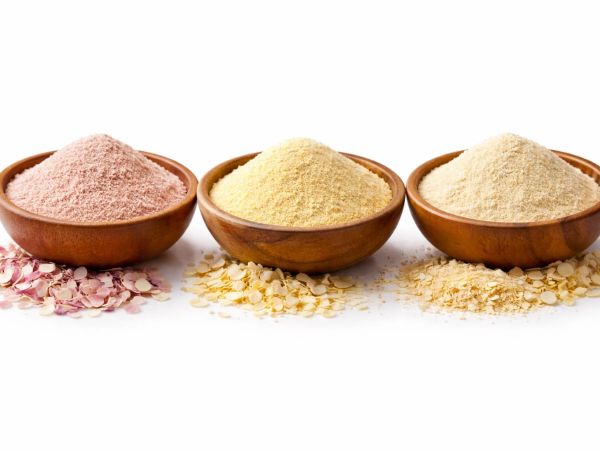 Three wooden bowls with different colored powders and flakes on a white background.