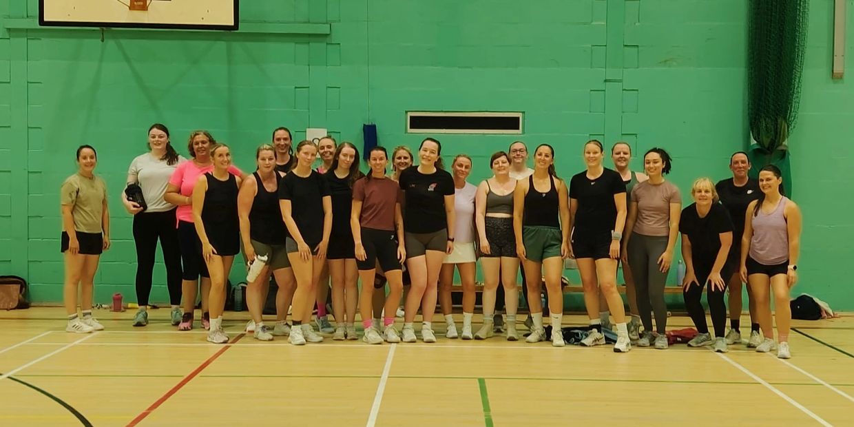 Group of women in gym attire posing in a sports hall.