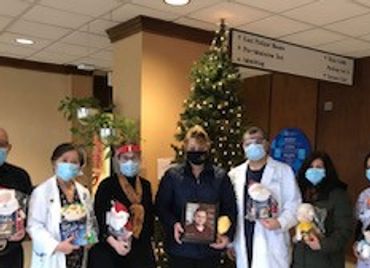 Group of healthcare workers in masks holding gifts by a Christmas tree.