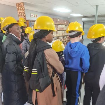 Group of people wearing yellow hard hats indoors, listening attentively.