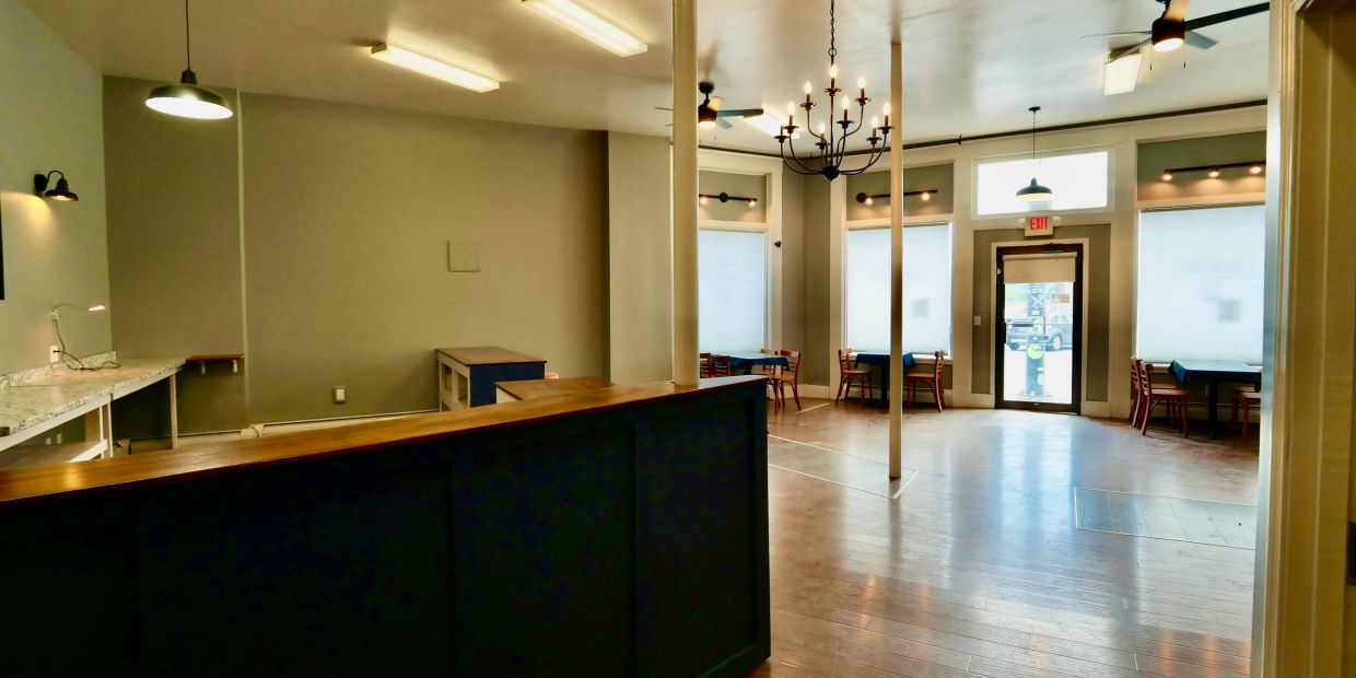 Empty room with wooden floors and tables by windows.
