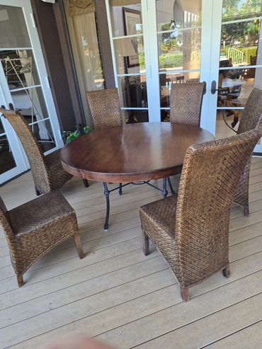 Outdoor wooden table with six wicker chairs on a porch.