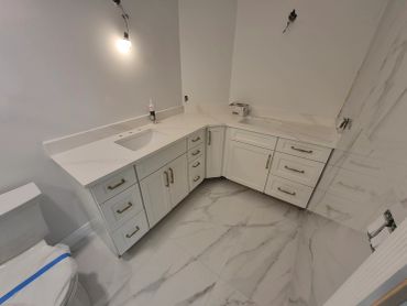Modern bathroom with white cabinetry and marble flooring under construction.