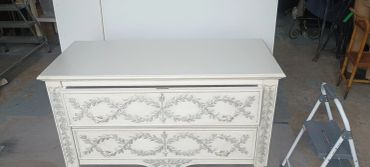 White dresser with intricate leaf and arrow carvings on drawers.