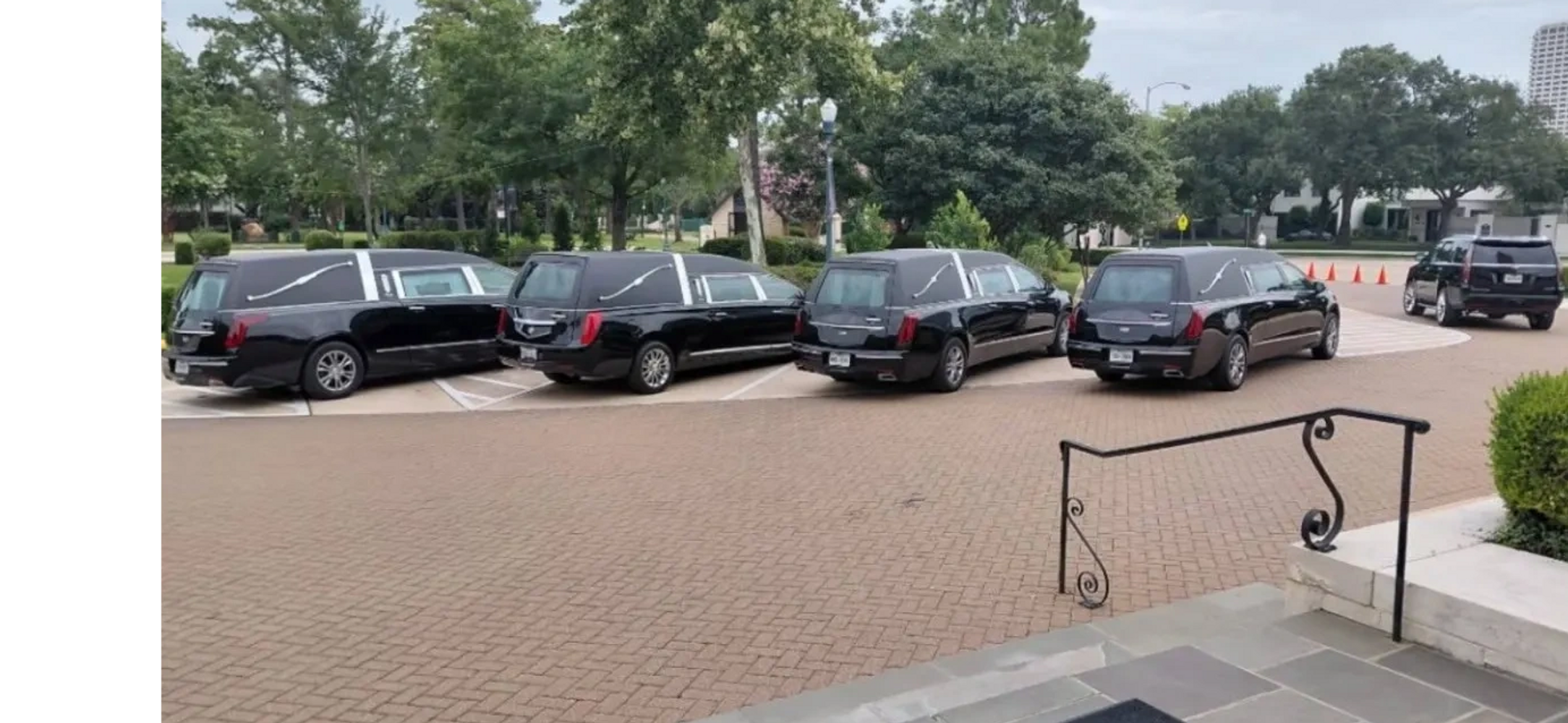 Four black hearses parked in a row outside a building on a cloudy day.