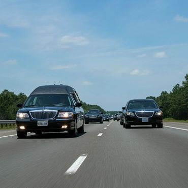 Black hearses and luxury cars driving on a highway in a funeral procession.