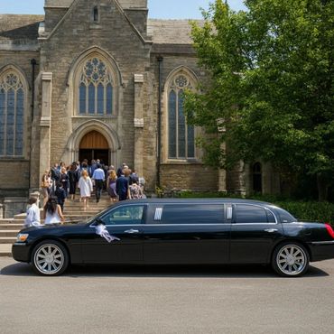 A black limousine parked in front of a church with people entering.