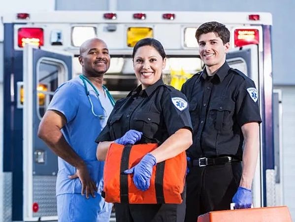 Three smiling paramedics standing confidently in front of an ambulance.