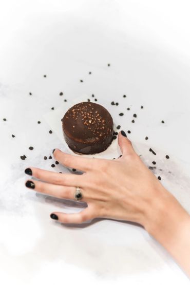Hand reaching for a chocolate dessert on a white surface.