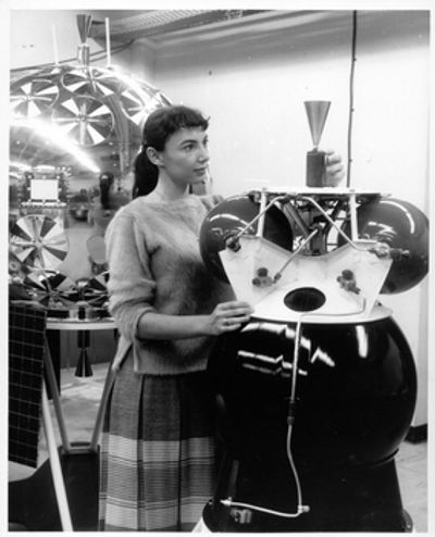 Woman examining early space exploration satellite equipment.