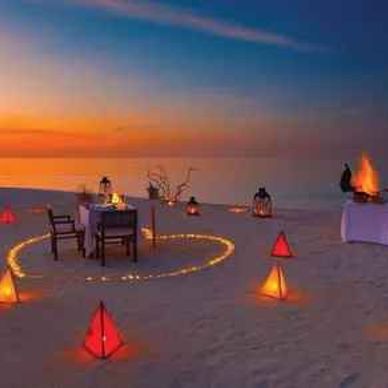 Romantic beach dinner setup at sunset with lanterns and candles.