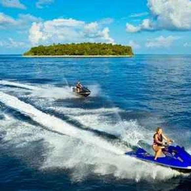 Two people riding jet skis near a tropical island under a blue sky.