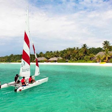 People sailing on a small boat in clear turquoise waters near a tropical island.