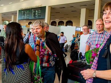People greeting each other at an airport arrival area with luggage.