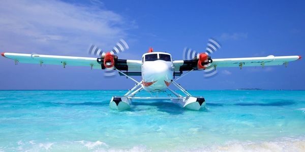 Seaplane with spinning propellers on clear turquoise water under a blue sky.