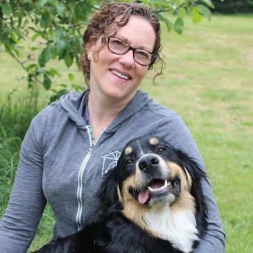 Woman smiling with a happy dog outdoors in a green park.