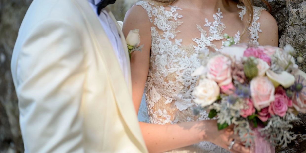 Bride and groom in elegant wedding attire holding a bouquet of flowers.