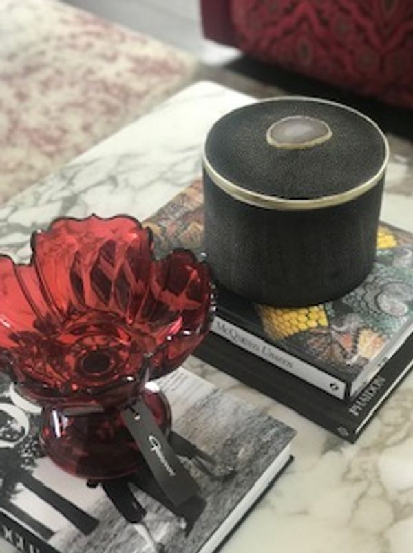 Decorative red glass bowl and black container on books with patterned covers.