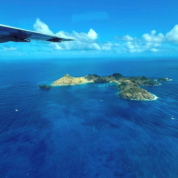 Aerial view of a small island surrounded by deep blue ocean with an airplane wing visible.