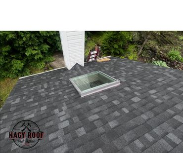 Newly installed gray shingle roof with a skylight and chimney.