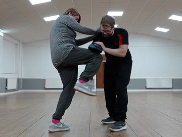 Woman practicing martial arts with pads indoors.