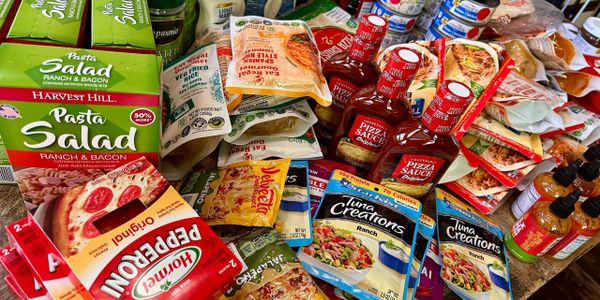 Various packaged food items including pasta salad, pepperoni, pizza sauce, and tuna creations.
