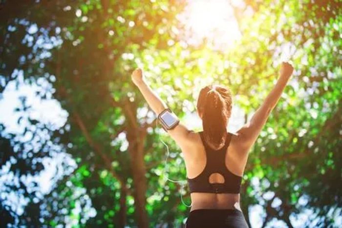 Woman celebrating outdoors with raised arms under sunlight.