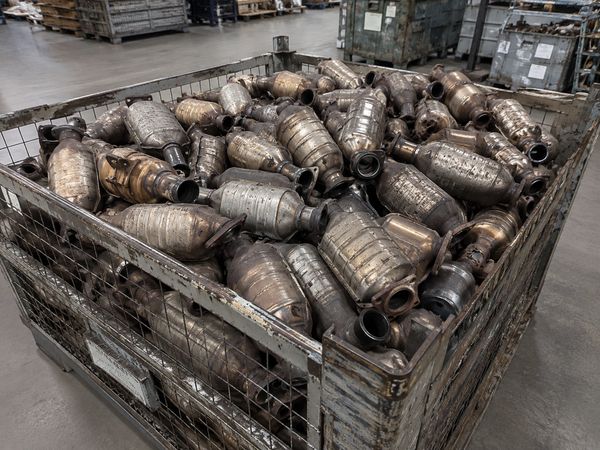A large metal container filled with used catalytic converters in a warehouse.