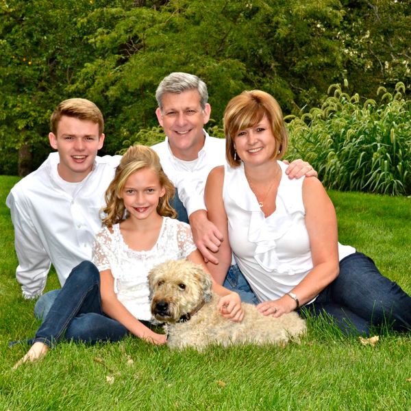 Smiling family of four with their dog sitting on green grass outdoors.