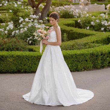 Bride in a white wedding gown holding a bouquet in a garden.