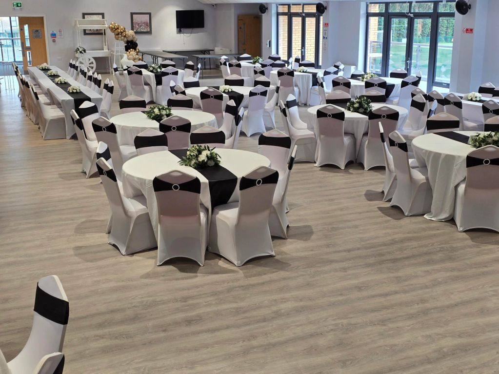 Elegantly decorated event hall with white and black chair covers and floral centerpieces.