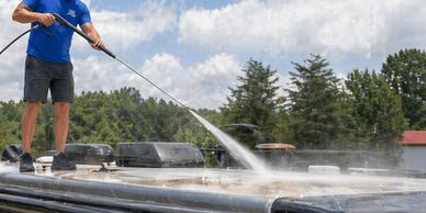 A man power washes the roof of an RV on a sunny day.