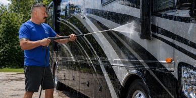 A man power washes a large RV on a sunny day.