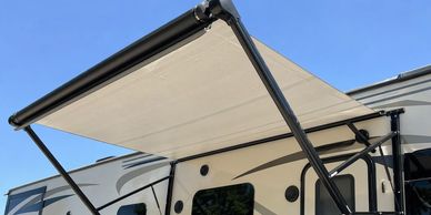 Retractable awning extended on the side of an RV under a clear blue sky.