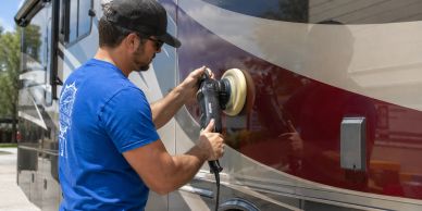 Man polishing the side of a recreational vehicle outdoors.