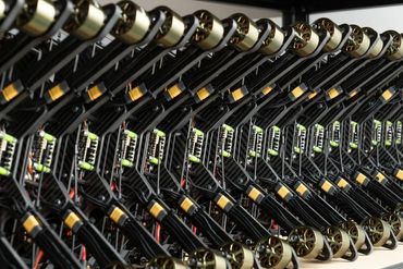Rows of identical drone arms with motors and wiring neatly arranged on a shelf.