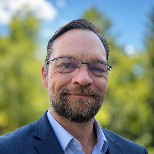 Smiling man in glasses and suit outdoors.