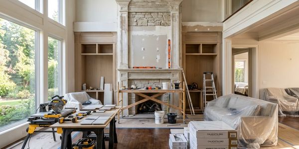 Living room under renovation with tools and covered furniture.