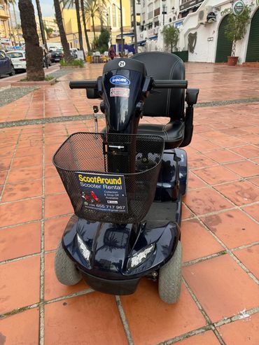 Electric mobility scooter with rental advertisement parked on a tiled sidewalk.