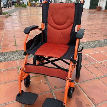Orange and black wheelchair on a tiled outdoor patio.