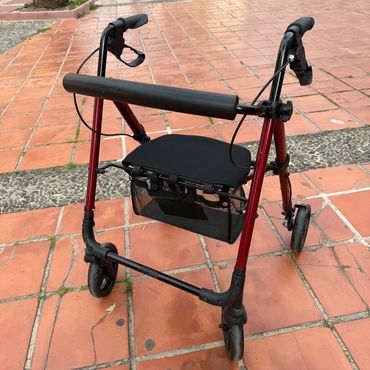 A red and black walker with a seat and basket on a tiled sidewalk.