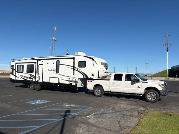 White pickup truck towing a large Sabre travel trailer in an empty parking lot.