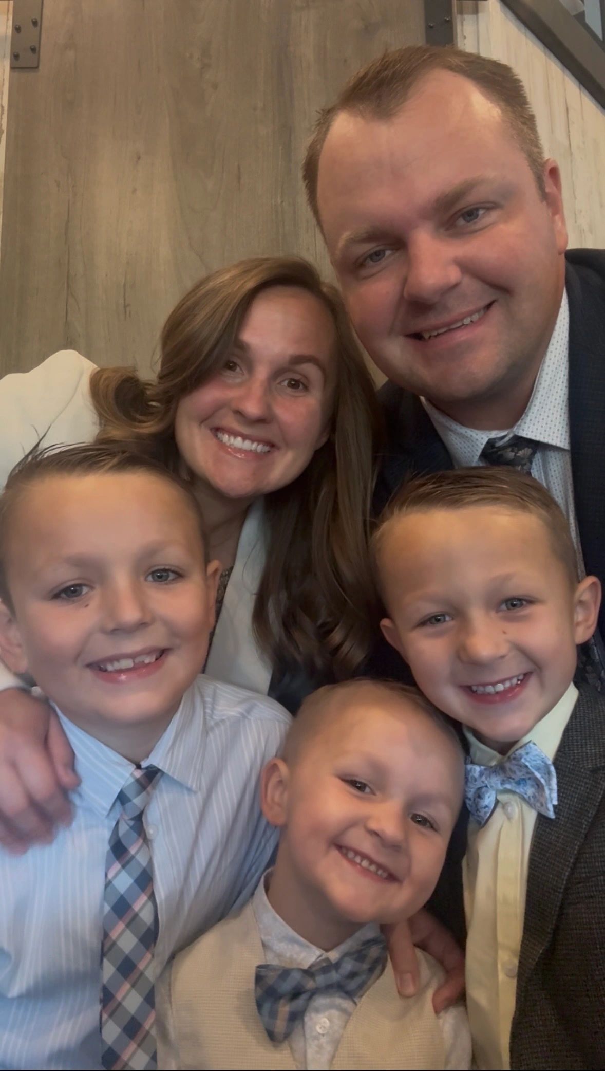 A happy family of five dressed formally, smiling at the camera indoors.